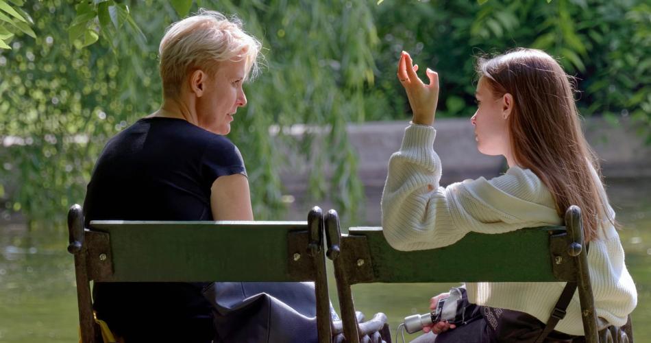 Frau und Mädchen sitzen auf einer Bank und reden miteinander